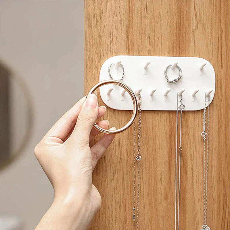 Jewelry Storage - Hand placing a gold bangle on the mounted organizer, with rings and necklaces hung on adjacent pegs on a wood surface