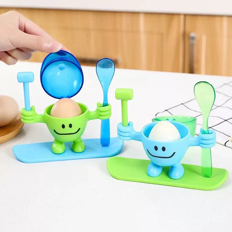 Egg Cup Holder - Two color variants of the character stand holding brown and white boiled eggs, with a hand lifting the cap on the green unit