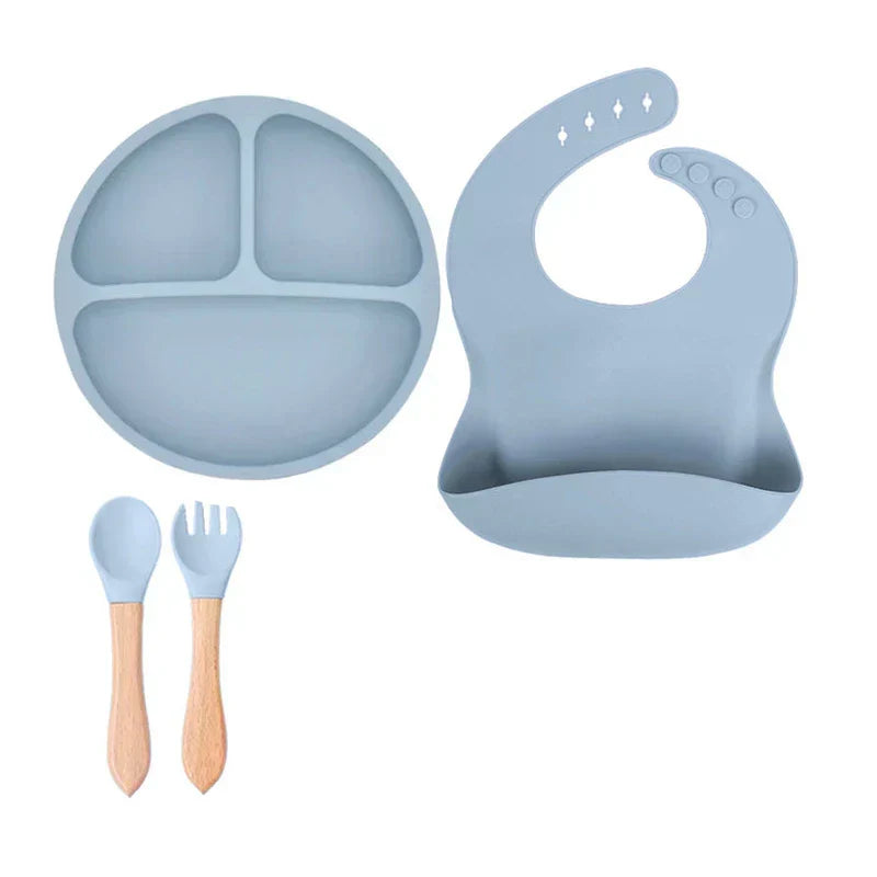 Cutlery Set - Light blue divided plate, adjustable bib, and wood-handled spoon and fork laid flat on white background