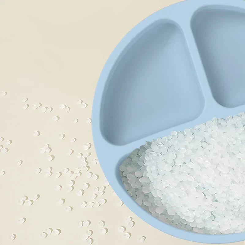 Cutlery Set - Close-up of a light blue divided silicone plate with small transparent pellets in one compartment, and scattered pellets on the adjacent beige surface.