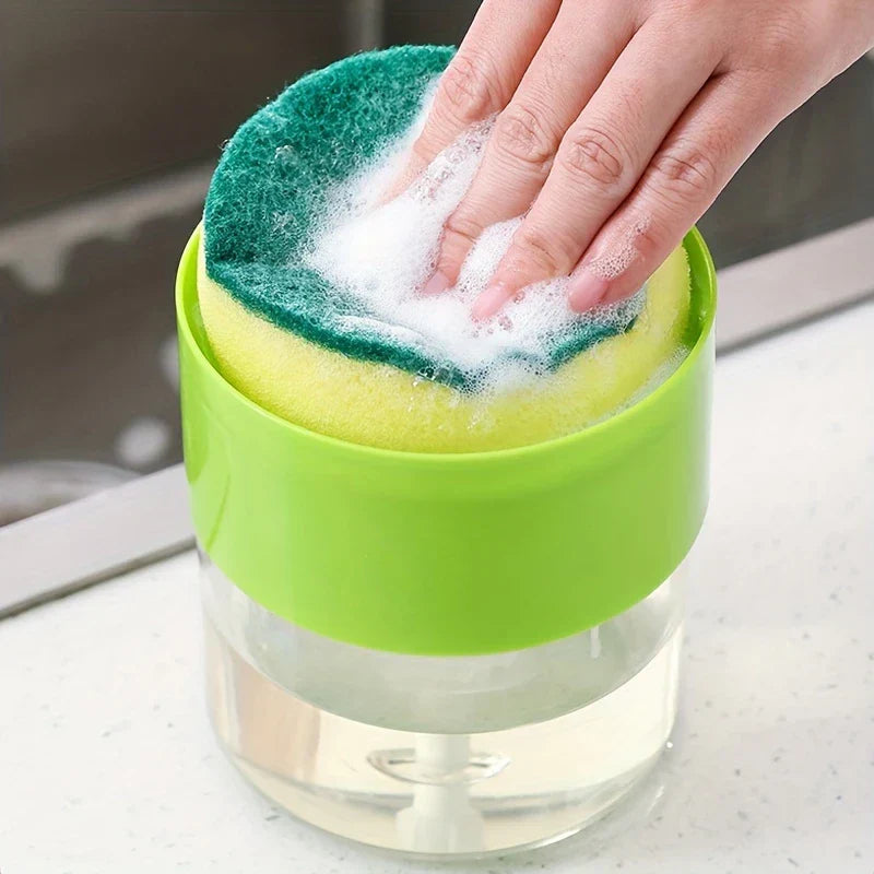 Kitchen Soap Dispenser Caddy - Hand pressing a soapy sponge on top of a green and clear kitchen soap dispenser placed on a countertop beside a sink