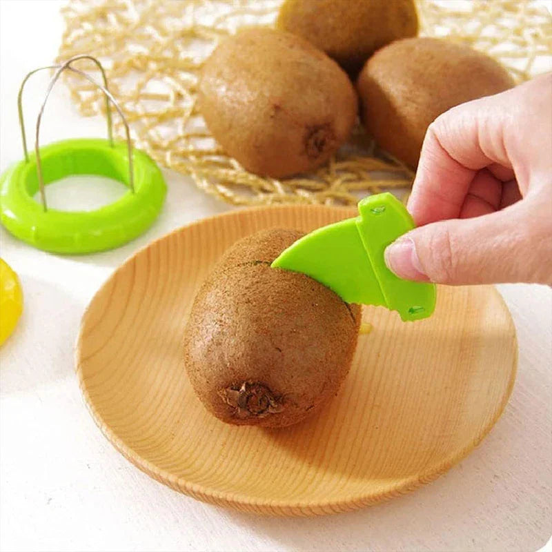 Kiwi Cutter Peeler Slicer Tool - Hand uses small green plastic cutter to score a whole kiwi on a wooden plate, with the loop tool and other kiwis in background