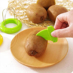 Kiwi Cutter Peeler Slicer Tool - Hand uses small green plastic cutter to score a whole kiwi on a wooden plate, with the loop tool and other kiwis in background