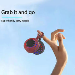 Portable Bluetooth Speaker - A hand holds two small portable speakers with integrated carry hooks, against a light blue sky background.