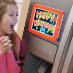 Drawing Board - Orange-framed glow drawing pad mounted on a fridge, screen displays neon 'Happy Birthday!' artwork; girl looks excited beside it