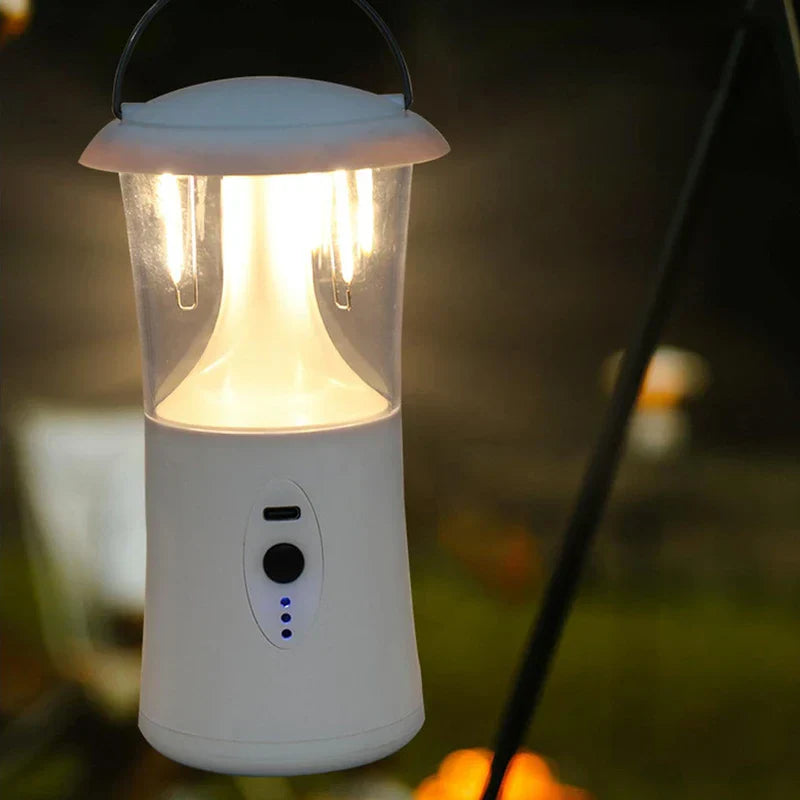 White camping lantern hanging, lit with warm light, three blue indicator LEDs visible on its control panel