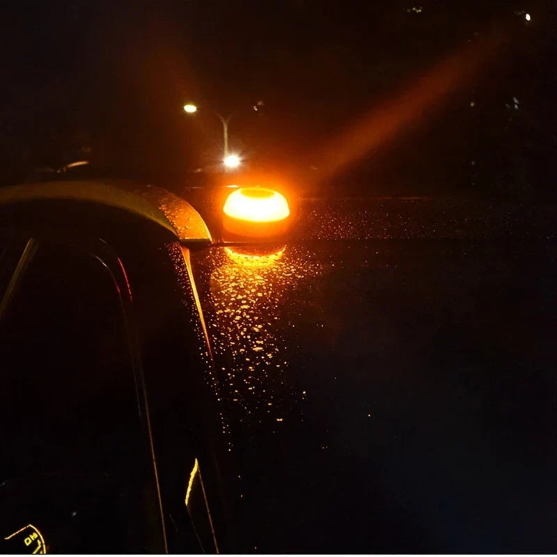 Warning Light - The orange and clear device lit up warm amber, mounted on a wet car window glass at night.