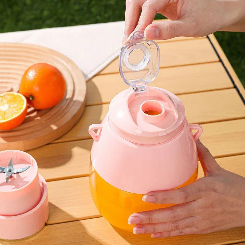 Blender Bottle - Hands opening the flip-top drinking spout on the pink juicer with orange juice inside, blade unit placed beside it on a wooden table