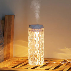 Cool Mist Humidifier - The diamond-textured transparent cylinder sits on a wooden slatted surface, emitting white mist from its top and glowing with warm yellow light, with a white power cord connected and placed on the surface.