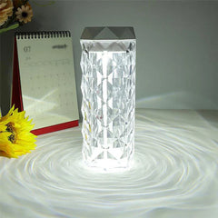 Cool Mist Humidifier - Clear faceted table lamp glowing white, casting circular light patterns on a white surface, with a desk calendar and sunflower to its left