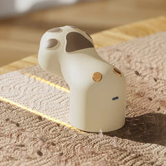 Sweater Fabric Defuzzer Machine - Cream cat paw shaped defuzzer resting on textured woven fabric, showing USB-C charging port and gold control buttons