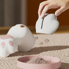 Sweater Fabric Defuzzer Machine - Hand lifting the removable blade cover of a light gray cat paw defuzzer, emptying collected lint clumps into a small pink dish