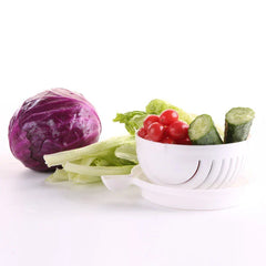 Juego de cuencos para servir: cuenco cortador de ensalada blanco con ranuras que contiene tomates cherry y trozos de pepino, colocado sobre su base, junto a repollo morado entero y lechuga