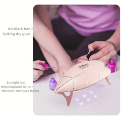 Lamp Uv Led Nail - Eine Person lackiert ihre Nägel, während eine kleine hellrosa UV/LED-Nagellampe auf dem Tisch neben drei Nagellackflaschen steht.