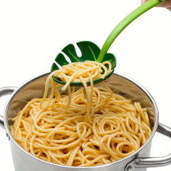 Strainer Spoon - Hand holding a green monstera leaf slotted spoon lifting cooked spaghetti from a stainless steel pot
