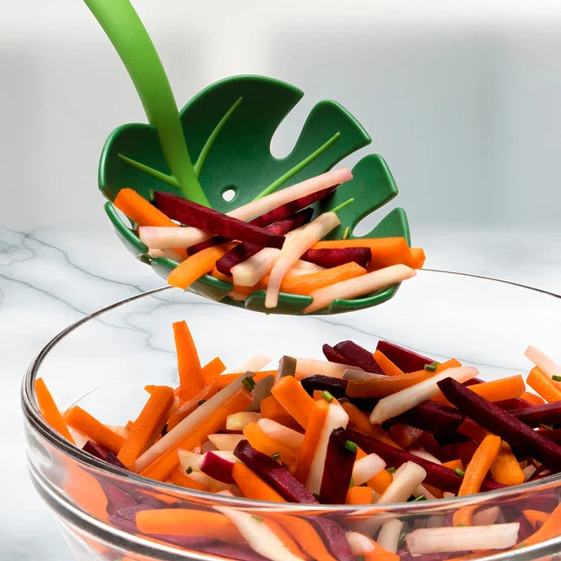 Strainer Spoon - Green monstera leaf slotted spoon holding cut vegetable strips above a glass bowl of mixed vegetables