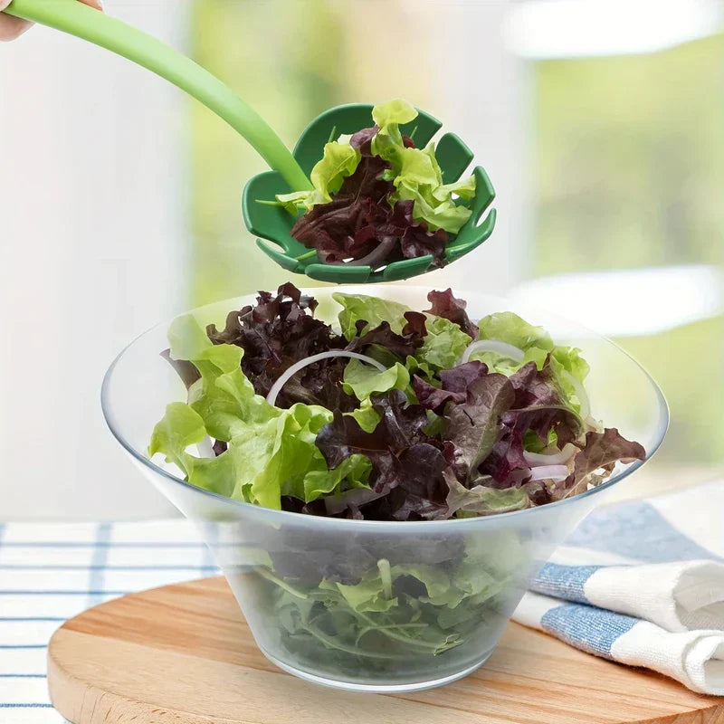 Strainer Spoon - Green slotted salad serving spoon lifts mixed lettuce from a clear glass salad bowl on a wooden board