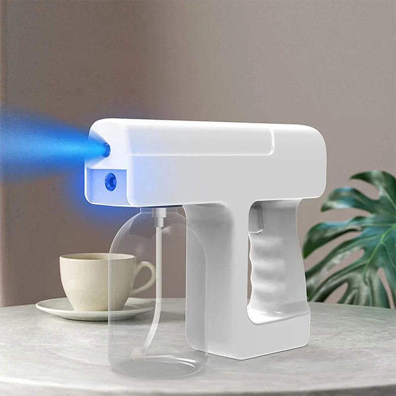 Mist Spray Bottle - Handheld atomizer emitting fine blue-tinted mist, placed on a light stone tabletop beside a ceramic teacup and houseplant