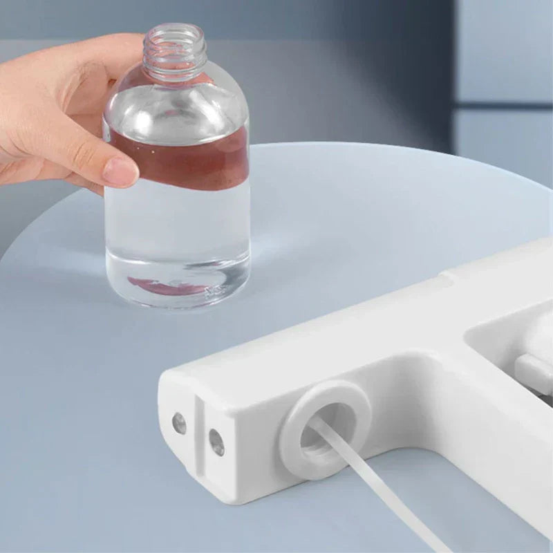 botella pulverizadora de niebla - Mano sostiene una botella de líquido transparente junto a un dispositivo pulverizador blanco parcialmente visible sobre una superficie azul claro