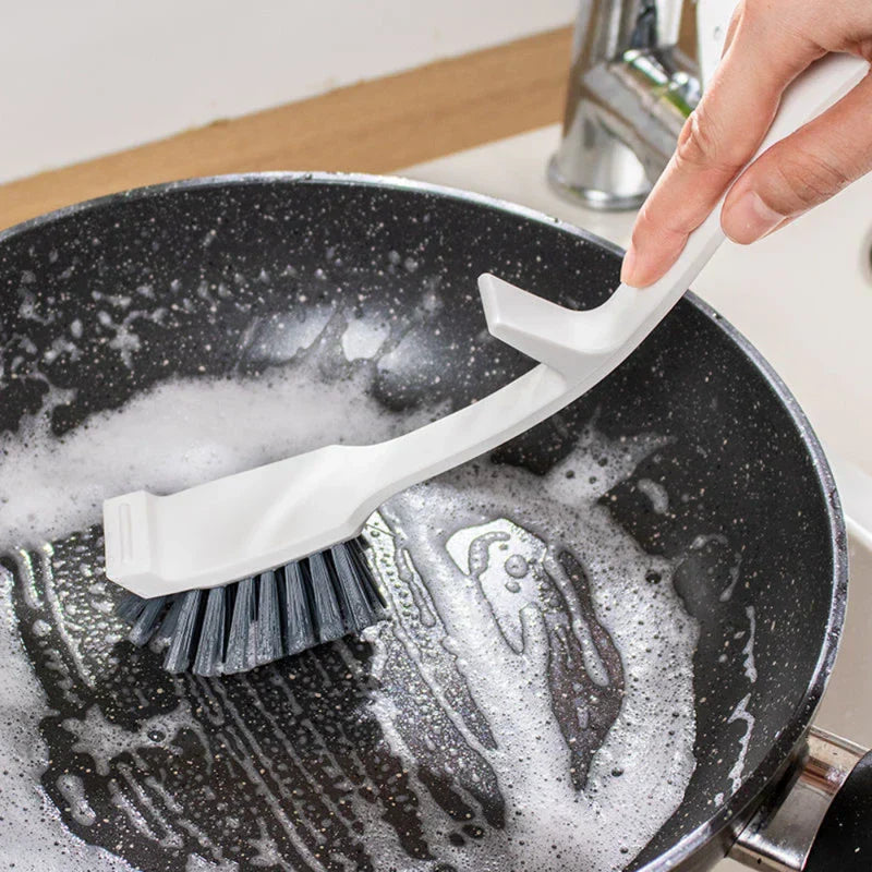 flaschenreinigungsbürste mit langem griff - Hand hält eine weiße Geschirrbürste und schrubbt das Innere einer gesprenkelten schwarzen Pfanne mit Seifenwasser