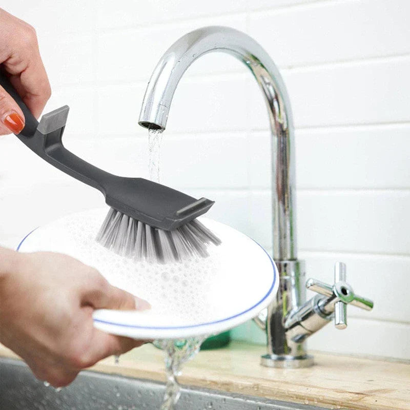 flaschenreinigungsbürste mit langem griff - Schwarze und graue Geschirrbürste unter fließendem Wasser, während ein weißer Teller mit blauem Rand geschrubbt wird