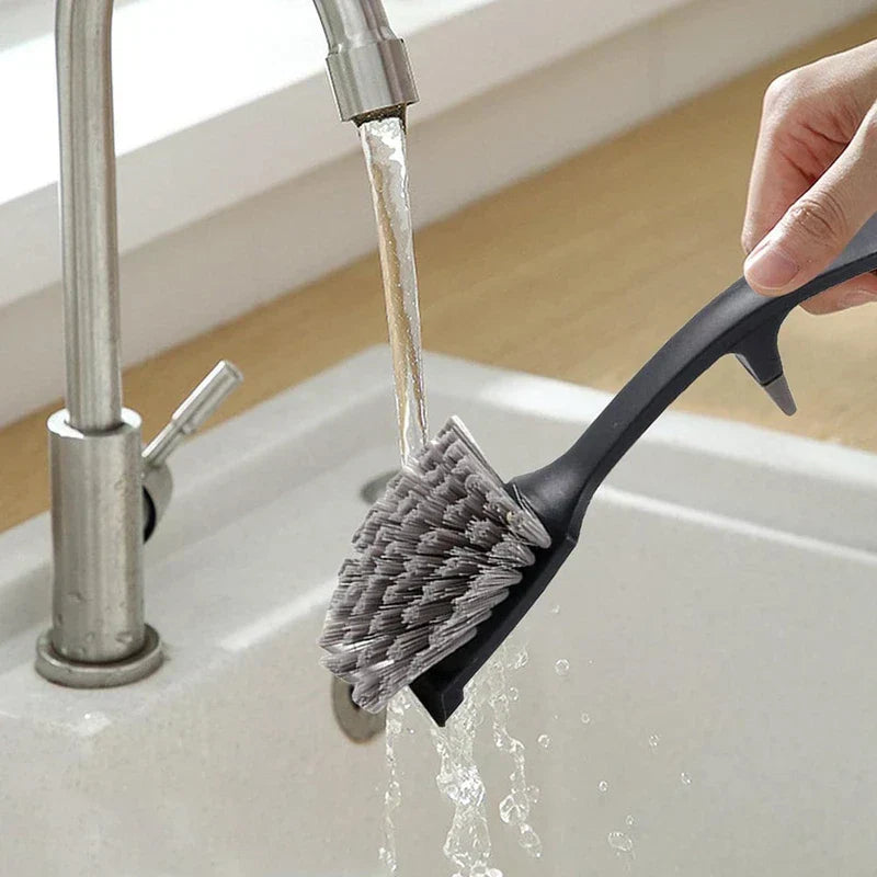 flaschenreinigungsbürste mit langem griff - Hand hält eine Geschirrbürste mit schwarzem Griff und spült ihre grauen Borsten unter fließendem Wasser an einem weißen Waschbecken aus