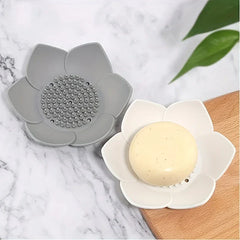 Soap Dish Holder - Gray and white lotus-shaped holders displayed on marble and wood surfaces, one holding a round bar of soap