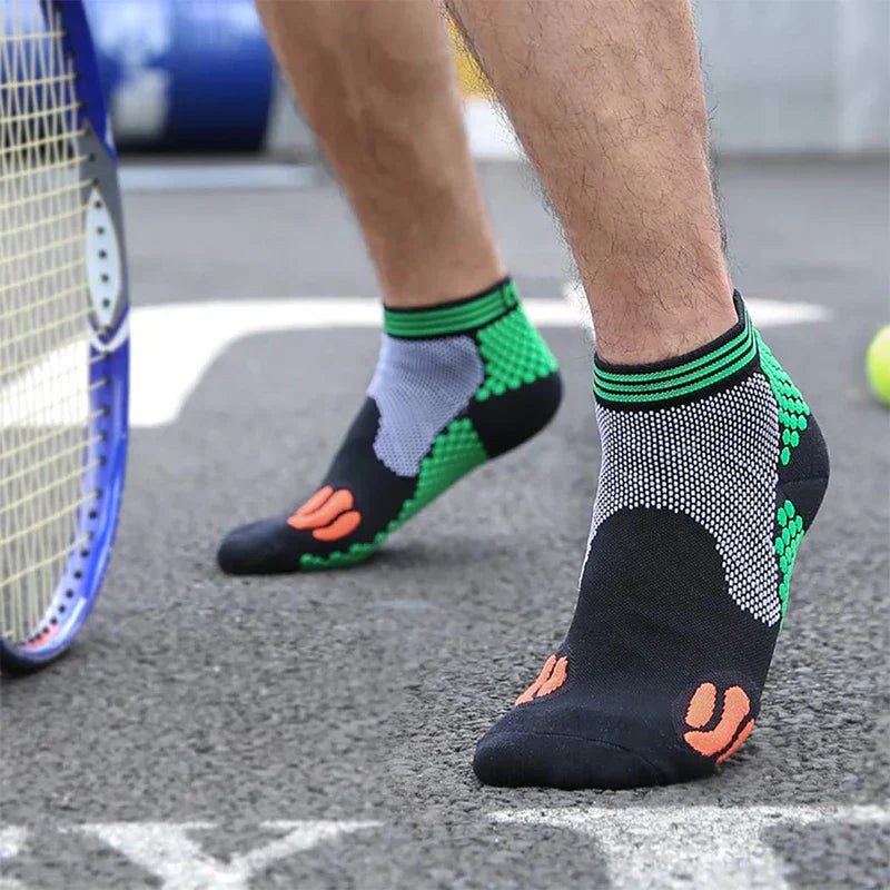 Casual Socks Pack - Person standing on a paved tennis court wearing black, green, white and orange short athletic socks, with a tennis racket and ball nearby