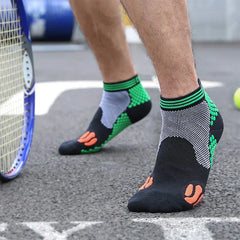 Casual Socks Pack - Person standing on a paved tennis court wearing black, green, white and orange short athletic socks, with a tennis racket and ball nearby