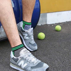 Casual Socks Pack - Person’s lower legs and feet wear gray sneakers with black green-trimmed ankle socks, two tennis balls lie on dark pavement nearby.