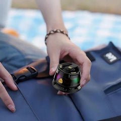 Floating Speaker - Hand holding a small black speaker with colored LED lights, resting over blue fabric with another hand holding the fabric edge.