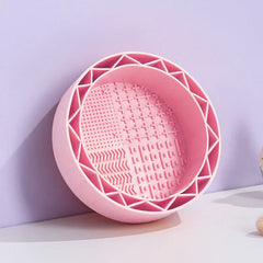 Makeup Brush Cleaning Mat - Light pink silicone cleaning bowl resting against a light purple background, showing its full interior textured surface and edge slots