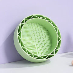 Makeup Brush Cleaning Mat - Light green round silicone bowl with textured interior patterns, placed against a light purple background on a white surface