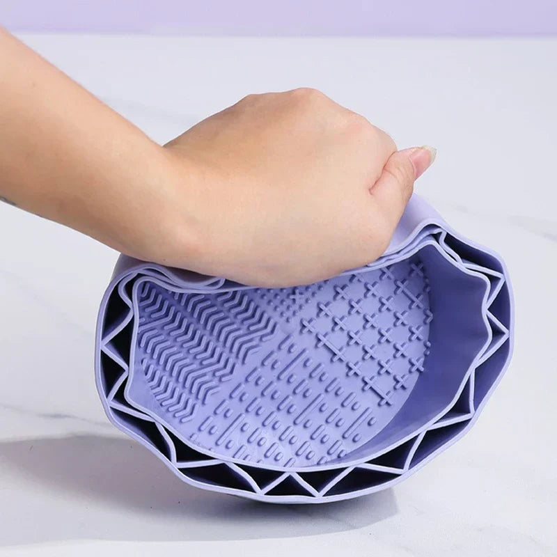 Makeup Brush Cleaning Mat - Hand squeezing a light purple flexible silicone cleaning bowl, showing its textured interior with multiple raised pattern zones