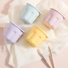 Makeup Brush Set - Four pastel lidded containers arranged on white fabric, with two small makeup brushes placed nearby