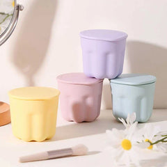 Makeup Brush Set - Four pastel lidded containers sit on a white surface with daisies and a makeup brush nearby, a mirror at left.