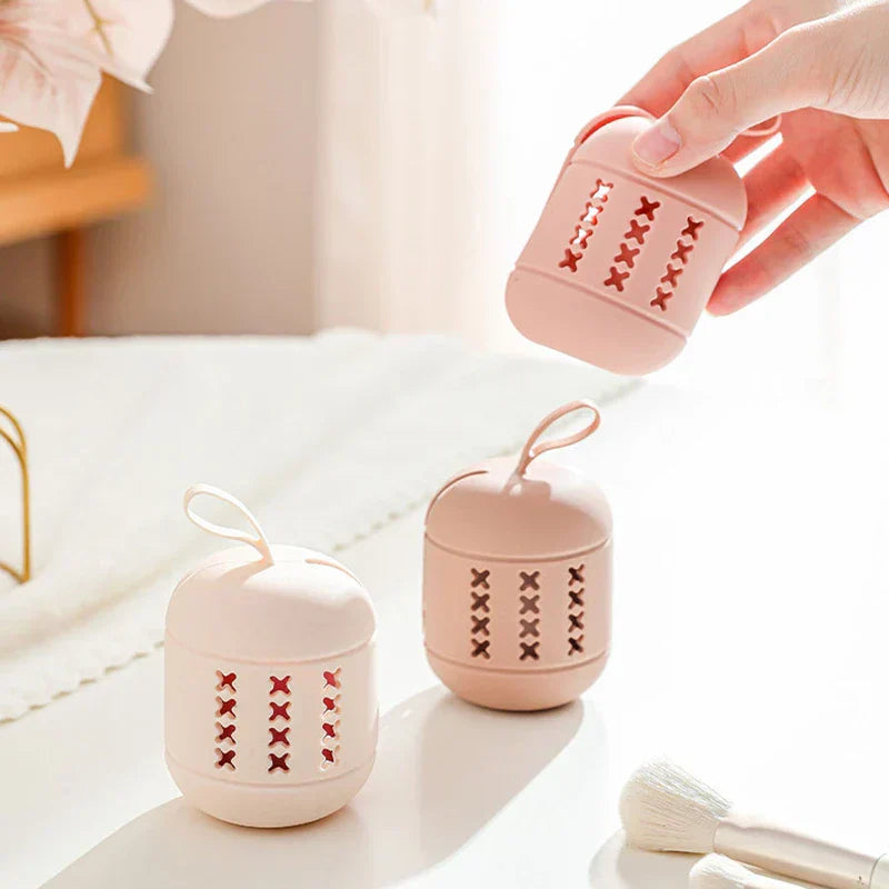 Hand holding a pink ventilated beauty sponge holder above two matching stands on a white vanity counter