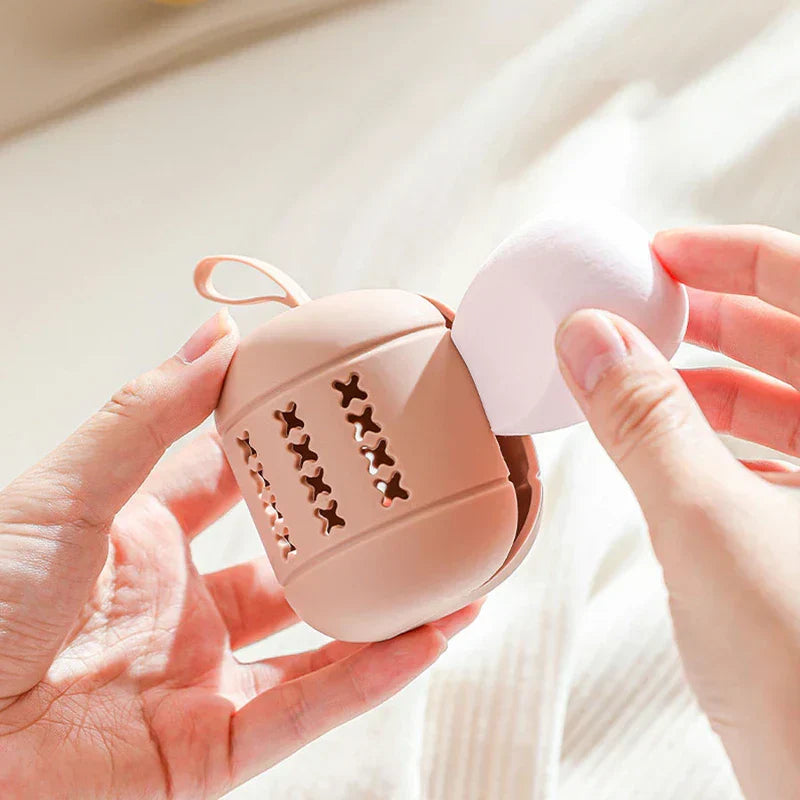 Eine Hand hält einen offenen rosa Make-up-Schwammhalter, während eine andere Hand einen weißen Make-up-Schwamm in der Nähe hält.