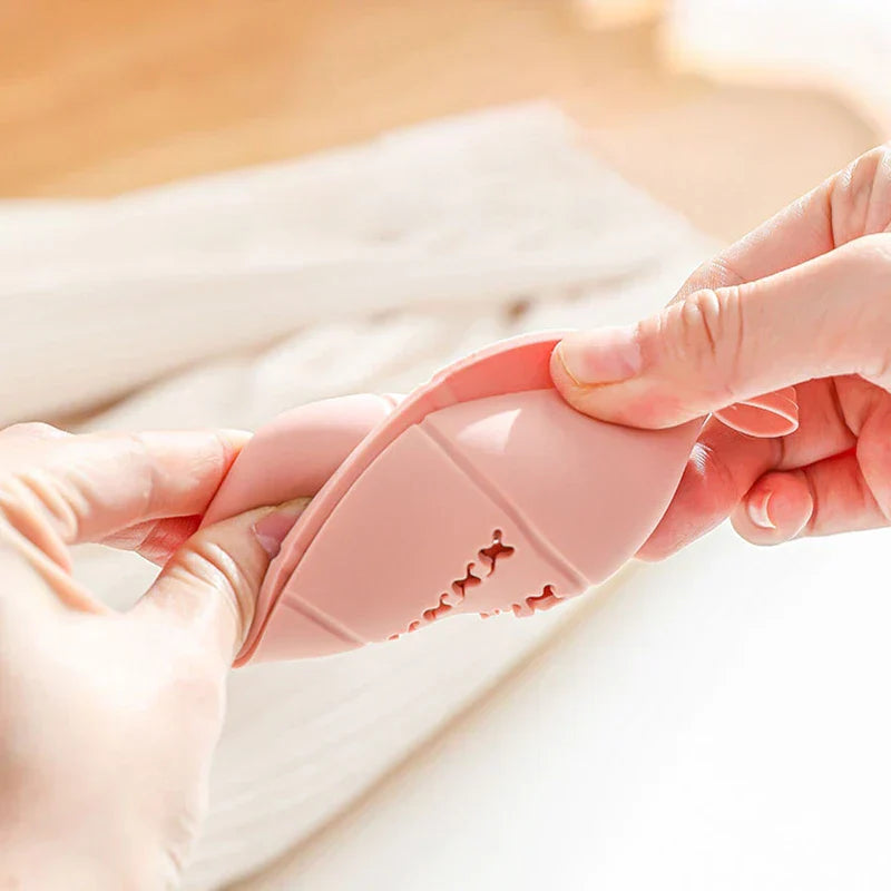 Deux mains pressent un support flexible rose avec des découpes en X ; la forme complète du support de éponge de maquillage n’est pas entièrement visible