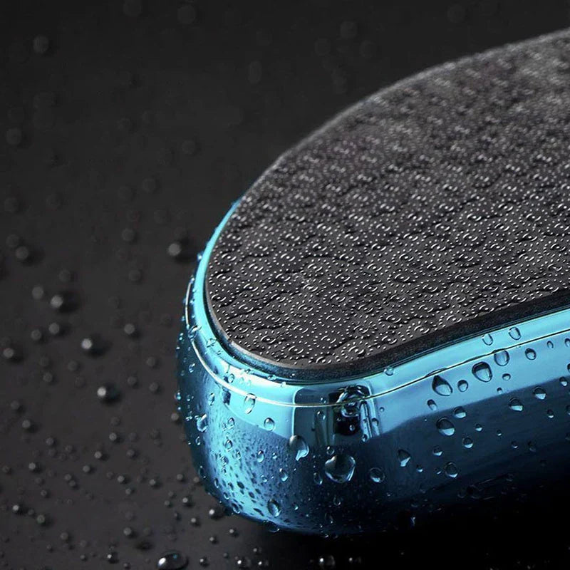Exfoliador de callosidades: vista parcial en ángulo de un dispositivo azul y negro cubierto de gotas de agua sobre una superficie oscura y húmeda