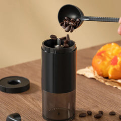 Coffee Bean Grinder - Black manual coffee grinder with lid removed, coffee beans being poured into its opening from a scoop
