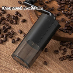 Moulin à café - Moulin à café manuel noir couché sur le côté sur une surface en bois parsemée de grains de café, avec un texte indiquant son silo à poudre transparent