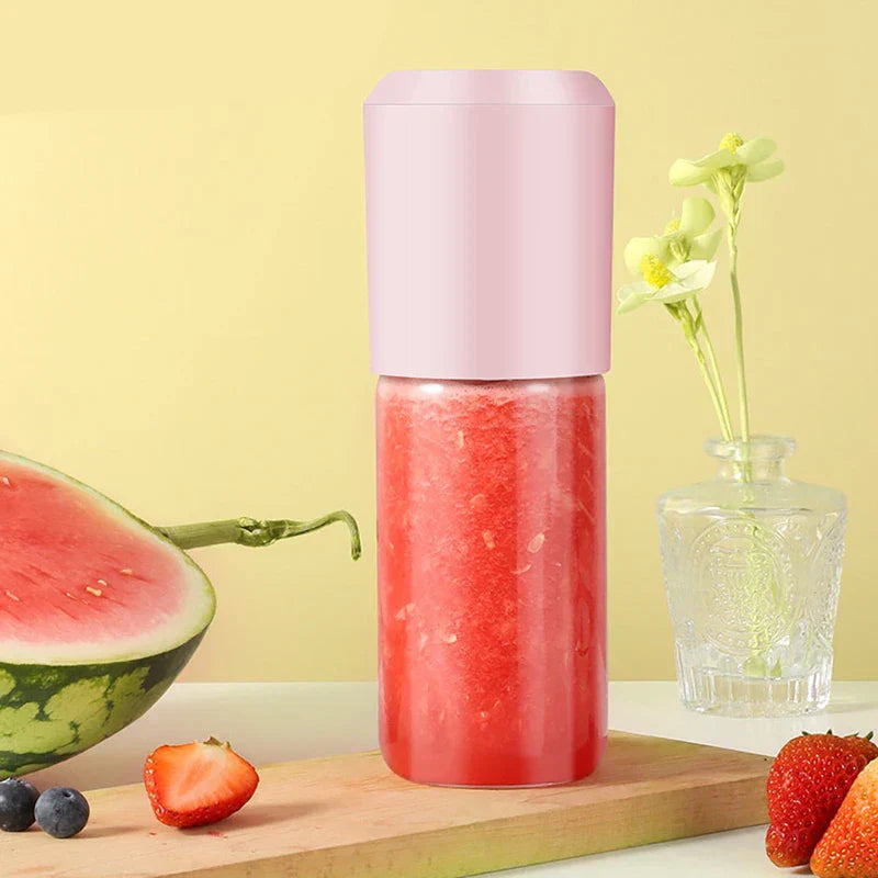 Pink portable blender with fresh watermelon juice on wooden board, fruits and flowers nearby
