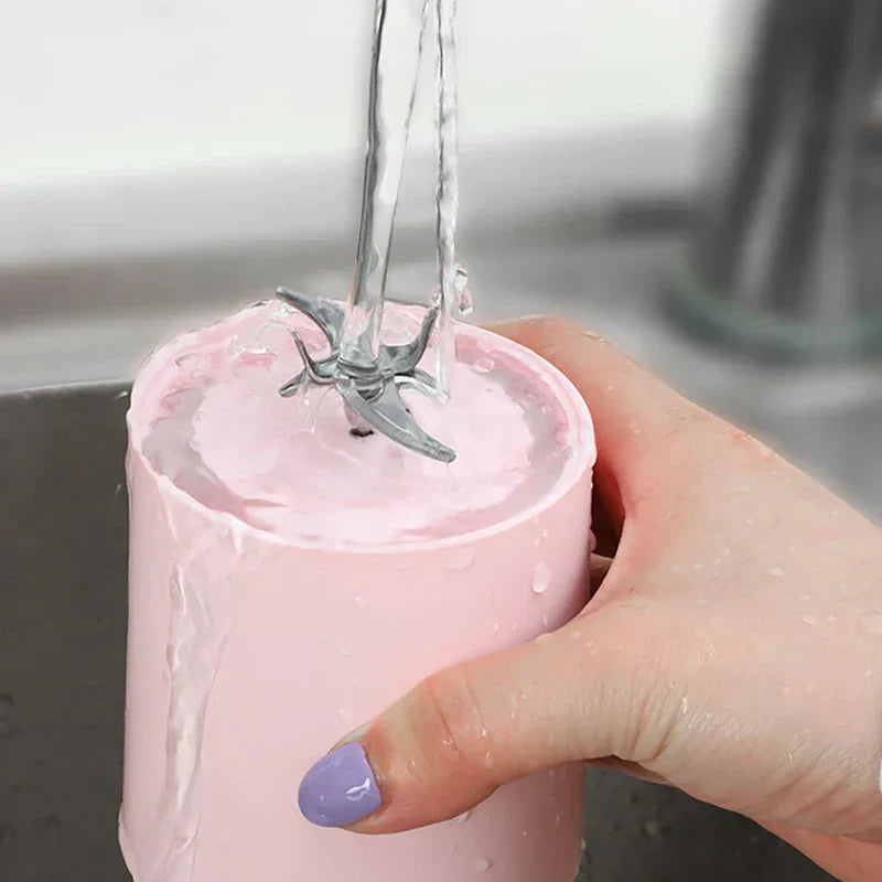 Pink portable juicer blender blade base being rinsed under running water