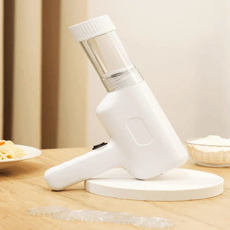 Manual Pasta Maker - White handheld kitchen tool resting on a round white display stand on a light wood table, with a plate of plain noodles and small bowl of flour placed nearby