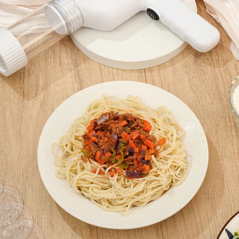 Manual Pasta Maker - White handheld cordless noodle maker resting on a round white base, alongside a bowl of homemade sauce-topped noodles on a wood table.