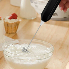 Whisk Mixer - Handheld mixing tool being used to whip egg whites in a clear glass bowl, with frosted cupcakes visible in the background