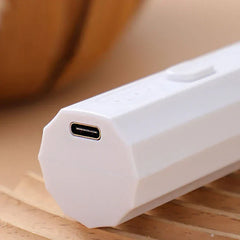 Whisk Mixer - Close-up of the angled USB-C charging end of a white handheld electric device, resting on a slatted wood surface