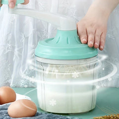 Manual Rotary Hand Whisk Egg Beater - Two hands turning the rotary whisk's crank, with motion effects around the container, eggs placed beside it on the table.