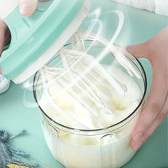 Manual Rotary Hand Whisk Egg Beater - Two hands hold a manual whipped cream maker over a glass container of frothy white cream, with the rotating beaters visible in motion.